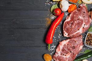 Raw pork meat on wooden cutting board at kitchen table for cooking pork steak roasted or grilled with ingredients herb and spices , Fresh pork. photo