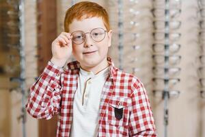 Handsome boy choosing glasses at optics store. health care and vision concept photo