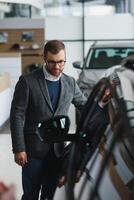 visitando coche concesión. hermoso barbado hombre es acariciando su nuevo coche y sonriente foto