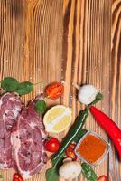 Raw pork meat with spices and vegetables on wooden table. photo