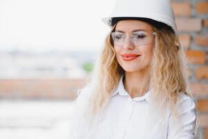 construcción ingeniero. niña con construcción documentación. un mujer en un blanco difícil sombrero en contra el techo de un edificio. construcción de un nuevo casa. foto