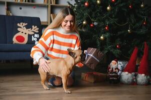 hermosa niña sentado en el sofá con un perro en el antecedentes de Navidad foto