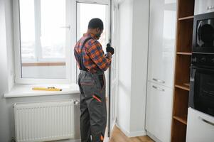 Workman in overalls installing or adjusting plastic windows in the living room at home photo