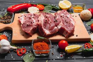 Raw pork meat on wooden cutting board at kitchen table for cooking pork steak roasted or grilled with ingredients herb and spices , Fresh pork. photo