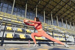 deporte y bienestar. aptitud niña haciendo extensión ejercicio. Moda deportivo mujer con fuerte muscular cuerpo capacitación. ajuste hembra extensión a al aire libre estadio foto