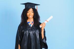 African-American beautiful woman in a black robe and hat, on a blue isolated background smiles. photo