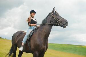 joven mujer montando un caballo en el verde campo foto