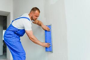 Portrait of a worker in overalls and holding a putty knife in his hands against the plastered wall background. Repair work and construction concept photo