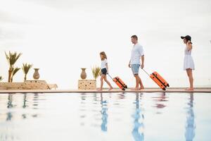 Young couple going to hotel through swimming pool upon arrival, looking for room, holding suitcases photo