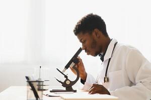 Portrait of young African-American man looking in microscope while working on medical research in laboratory, copy space. photo