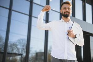 Real estate agent holding key on blurred background, closeup photo