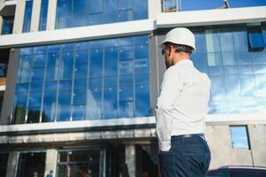 Engineer next to building cranes. Concept - large construction project. Architect directs the construction process. Drawings and tablet in the hands. photo