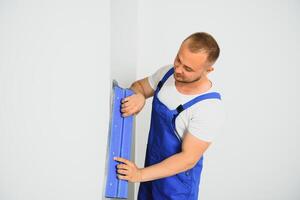 The builder carefully corrects the irregularities of the wall with a trowel. Builder in work clothes against a gray wall. Photo plasterer at work.