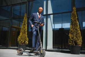 businessman with electric scooter standing in front of modern business building talking on phone. photo