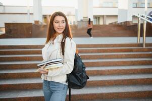 Young girl student smiling against university. Cute girl student holds folders and notebooks in hands. Learning, education concept photo