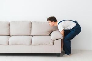 Loader moves sofa, couch. worker in overalls lifts up sofa, white background. Delivery service concept. Courier delivers furniture in case of move out, relocation. photo