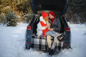 Smiling together. Nice couple have weekend at countryside at winter time. Sitting on the rear part of modern car. photo
