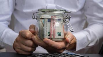 Euro Banknote Saving Money In Glass Jar. Unrecognizable man Moderate Consumption on calculator And Economy Collecting Money Tips Business Finance footage photo