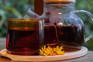 Calendula tea still life on table in green garden background. Healthy hot drink benefits. Natural organic aromatic drink in cup. Home-grown immunity-boosting herbs for tea. Autumn winter warming calming drink photo