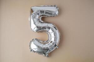 5 five metallic balloon on beige neutral background. Greeting card silver foil balloon number Happy birthday holiday concept. Copy space for text. Celebration party congratulation decoration photo