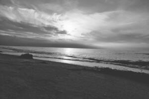 puesta de sol a el mar en negro y blanco soñador. arenoso playa en el primer plano foto