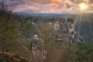 Jagged rocks at the Basteibridge. Wide view over trees and mountains. Dramatic sky photo