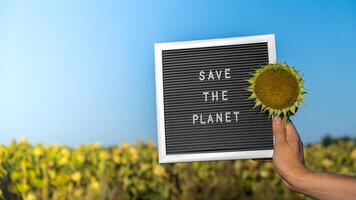 Unrecognizable person with banner message SAVE THE PLANET in sunflower field on sunny day. Sign EARTH day. Concept of ecology and eco activism environmental issues Stop global warming. Go green sustainable photo