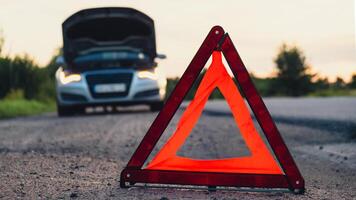 Unrecognizable sad driver in reflective vest. Male driver standing near broken car with open up hood. Red triangle to warn other road users of car breakdown or engine failure stop at countryside highway. Emergency traffic situation photo