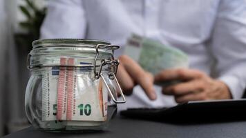 Man hands counting expenses banknotes of euro cash from glass jar in the piggy bank on calculator. Close up of hands unrecognizable Businessman. Save up budget investment concept. Euros fund savings footage photo