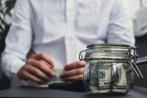 Dollar Banknote Saving Money In Glass Jar. Unrecognizable man calculate money on calculator Moderate Consumption And Economy Collecting Money Tips Business Finance concept photo