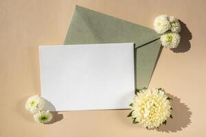 Composition with empty paper note and envelope beautiful spring white flowers on beige background. Mockup card invitation greeting card postcard copy space template. Blooming fresh natural flower. photo