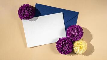 Composition with empty paper note and envelope beautiful spring violet and white flowers on beige background. Mockup card invitation greeting card postcard copy space template. Blooming fresh natural flower. photo