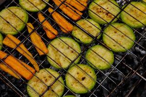 Chopped zucchini and carrots roasting on fire seasoned with aroma herbs and spices. Delicious fresh vegetables grilling on barbecue smoker grid. Diet vegan bbq. Outdoor recreation in backyard photo