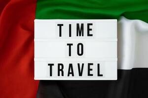 Message with text TIME TO TRAVEL on background of waving UAE flag made from silk. United Arab Emirates flag with concept of tourism and traveling. Inviting greeting card, advertisement. Dubai welcoming card photo