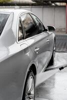 Washing luxury silver car on touchless car wash. Washing sedan car with foam self-service and high pressure water. Cleaning the details of car. Cleanliness and order in urban environment photo