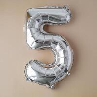 5 five metallic balloon on beige neutral background. Greeting card silver foil balloon number Happy birthday holiday concept. Copy space for text. Celebration party congratulation decoration photo