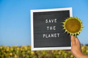 Hands of protester with text SAVE THE PLANET on black board on background of sunflower field. Reuse reduce recycle concept. Protesting for nature Climate strike volunteer protest against earth pollution, global warming photo