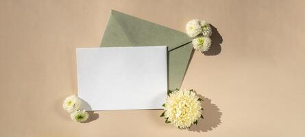 Beautiful little white flowers on postal green envelope on beige background, empty paper note copy space for text, spring time, greeting card for holiday. Flower delivery concept photo