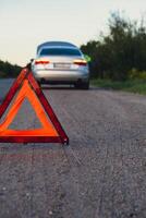 roto plata lujo coche emergencia accidente. hombre conductor instalando rojo triángulo detener firmar en la carretera. deporte automóvil convertido en anteojeras técnico problemas en el la carretera. la seguridad procedimiento cuando teniendo vehículo roto abajo foto