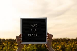 Hands of protester with text SAVE THE PLANET on black board on background of sunflower field. Reuse reduce recycle concept. Protesting for nature Climate strike volunteer protest against earth pollution, global warming photo