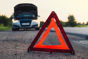 Broken silver luxury car emergency accident. Man driver installing red triangle stop sign on road. Sport automobile turned on blinkers technical problems on the road. Safety procedure when having vehicle broken down photo