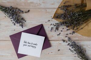 TAKE TIME TO MAKE YOUR SOUL HAPPY text on supportive message paper note reminder from green envelope. Flat lay composition dry lavender flowers. Concept of inner happiness, slowing-down digital detox personal fulfillment. Top view photo