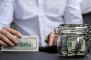 Dollar Banknote Saving Money In Glass Jar. Unrecognizable man calculate money on calculator Moderate Consumption And Economy Collecting Money Tips Business Finance concept photo