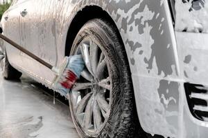 Lavado lujo plata coche en sin contacto coche lavar. Lavado sedán coche con espuma autoservicio y alto presión agua. limpieza el detalles de coche. limpieza y orden en urbano ambiente foto