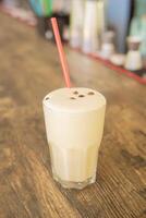 un frío café cóctel en un claro vaso con un Paja en un de madera bar mostrador foto