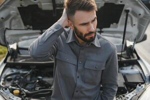 Sad driver holding his head having engine problem standing near broken car on the road. Car breakdown concept photo
