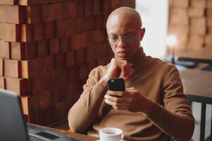 African businessman talking on phone sitting at cafe table, busy entrepreneur working distantly in coffee house with laptop papers speaking on mobile, black man making call having lunch in cafeteria. photo