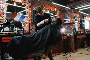 africano masculino cliente consiguiendo Corte de pelo a Barbero tienda desde profesional estilista. foto