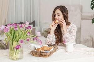 A brown-haired woman with long hair is having breakfast at the table with croissants and a cup of coffee. Spring portrait. photo