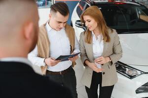 mature salesman showing new car to a couple in showroom. photo